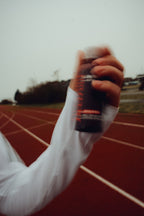 Athlete on running track holding beetroot energy shot bottle in hand