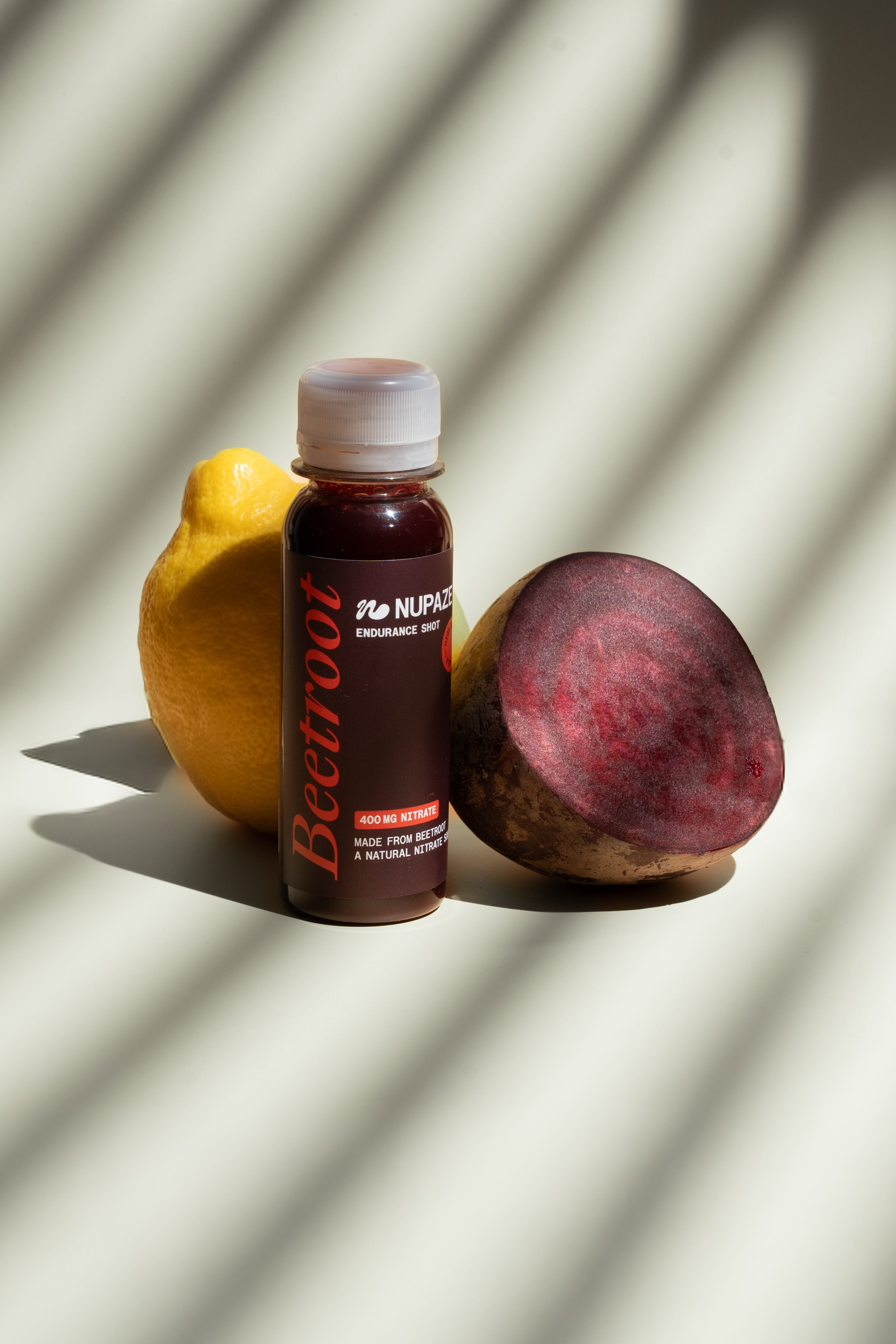 Beetroot shot bottle with beetroot half and lemon on neutral background, healthy drink